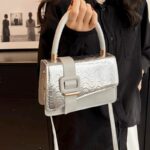 Femme élégante tenant fièrement le sac à main Gloria argenté, un accessoire scintillant pour un style sophistiqué.