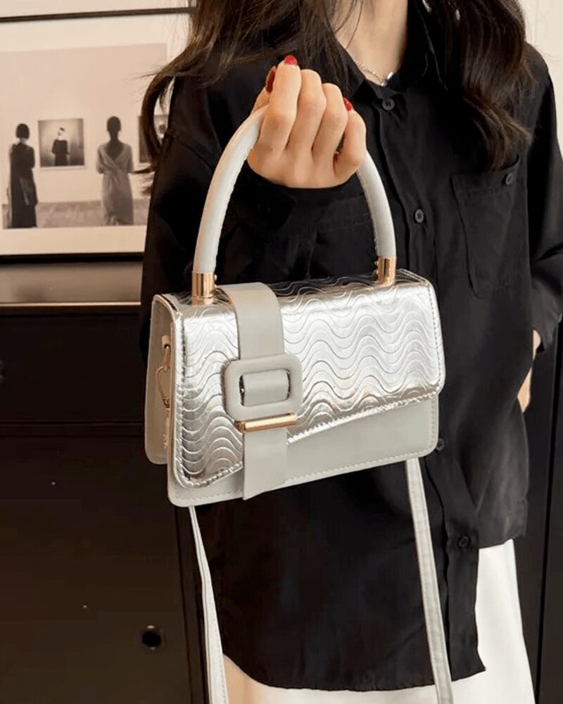 Femme élégante tenant fièrement le sac à main Gloria argenté, un accessoire scintillant pour un style sophistiqué.