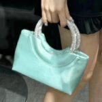 Myriam sac à main en satin vert, élégamment tenu par une femme.
