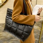 Découvrez le style inégalé de Maïssane avec son sac à main fourre-tout noir matelassé, porté avec élégance sur l'épaule par des femmes au raffinement distinct.