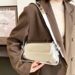 Laissez briller votre style avec le sac à main Molly en vernis argenté, une pièce raffinée et scintillante, tenue gracieusement à la main pour une allure sophistiquée.