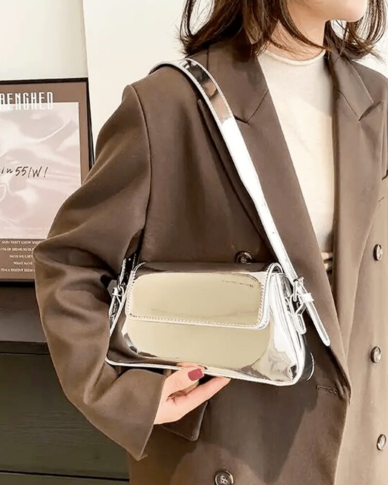Laissez briller votre style avec le sac à main Molly en vernis argenté, une pièce raffinée et scintillante, tenue gracieusement à la main pour une allure sophistiquée.