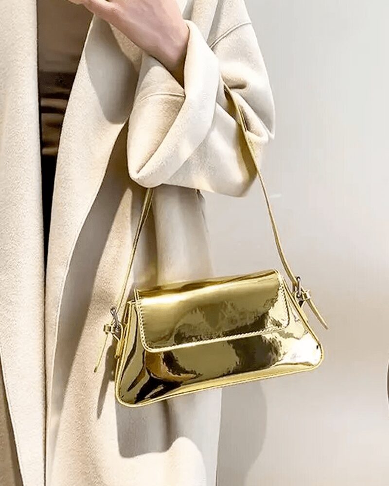 Faites briller votre style avec le sac à main Molly en vernis doré, une pièce luxueuse portée avec délicatesse au bras, ajoutant une touche glamour à votre look.