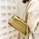 Illuminez votre style avec le sac à main Molly en vernis doré, une pièce luxueuse portée à l'épaule, pour une allure chic et glamour.