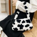 Sac à main motif vache Jamie en peluche, un accessoire élégant pour les femmes portant au bras.