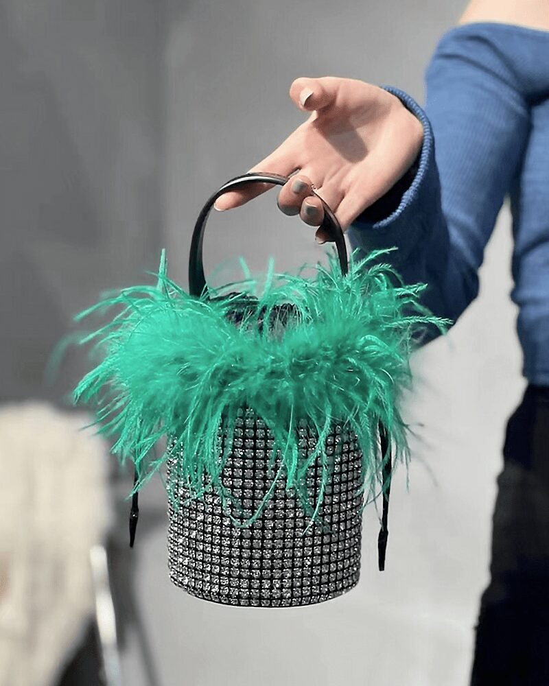 Élégance féminine incarnée : le sac à main Kendal, orné de strass et de plumes vertes, tenu avec grâce par une femme.