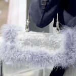 Élégance en mouvement : le sac à main Kylie, orné de strass et de plumes grises, porté avec style par une femme au bras.