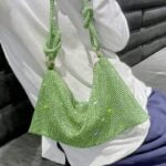 Sac à main vert orné de strass, porté à l'épaule, tenu par une femme.
