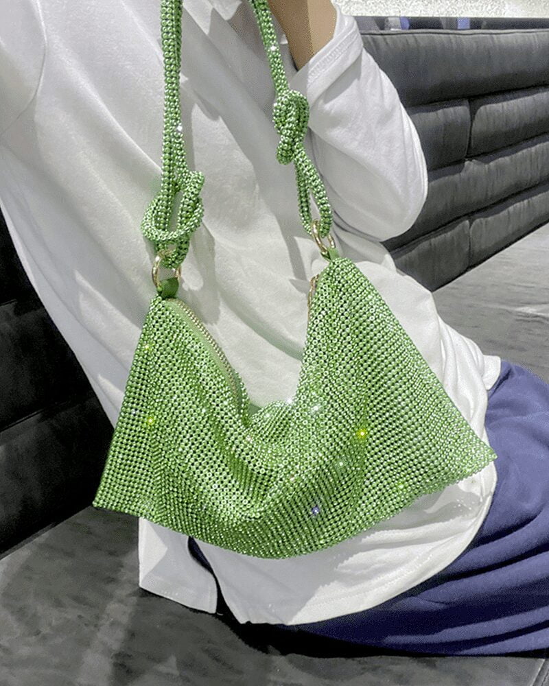 Sac à main vert orné de strass, porté à l'épaule, tenu par une femme.