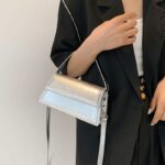 Sac à main Nawel argenté en similicuir brillant, porté sur le bras par une femme.