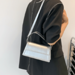 Sac à main Nawel argenté en similicuir brillant, porté sur l'épaule par une femme.