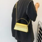 Sac à main doré Nawel en similicuir brillant, porté en bandoulière par une femme.