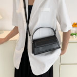 Sac à main Nawel noir en similicuir brillant, porté en bandoulière par une femme.