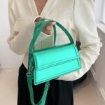 Femme tenant un sac à main Nawel vert en similicuir brillant.