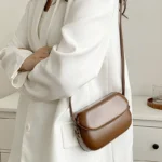 Sac à main Emy en similicuir marron porté à l'épaule par une femme, disponible chez Boutique Izamel.