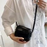 Sac à main Emy en similicuir noir avec bandoulière, porté par une femme, disponible chez Boutique Izamel.