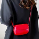 Sac à main Emy en similicuir rouge avec bandoulière, porté par une femme, disponible chez Boutique Izamel.
