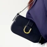 Sac à bandoulière noir vernis Inaya porté à l'épaule par une femme"