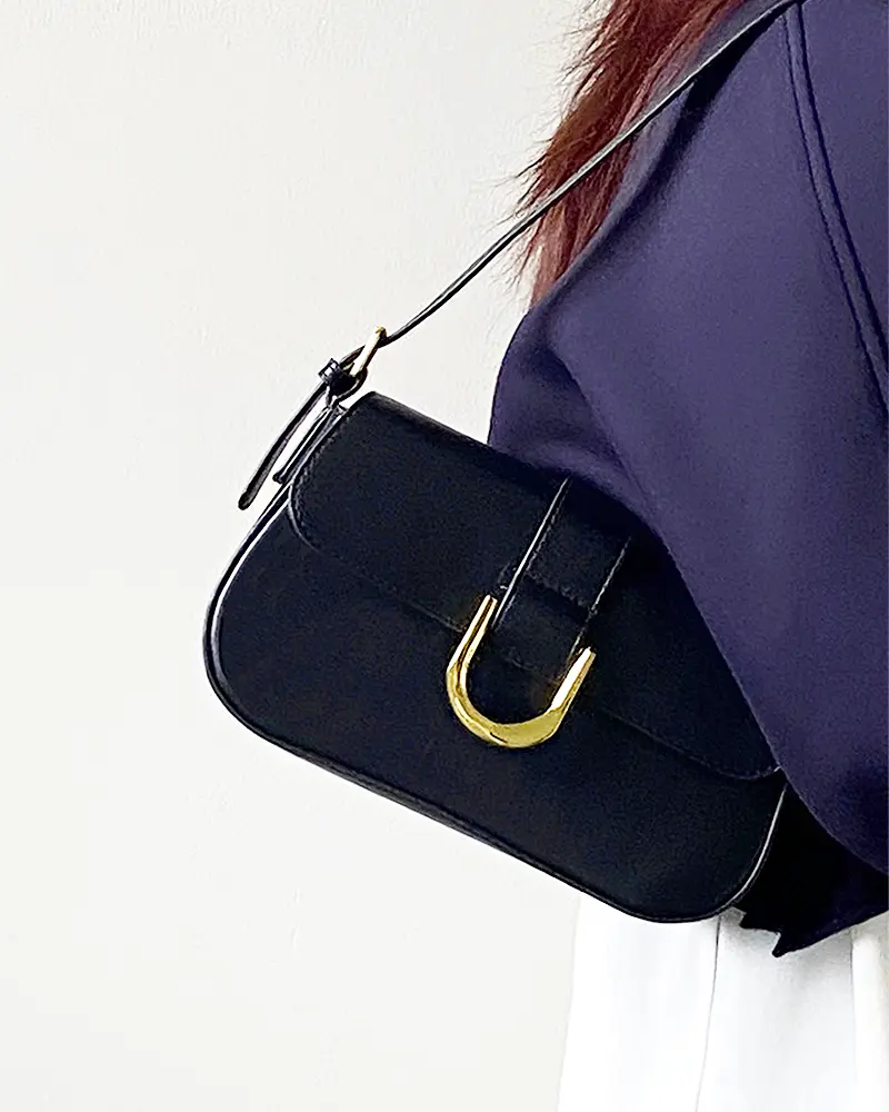 Sac à bandoulière noir vernis Inaya porté à l'épaule par une femme"