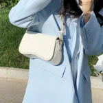 Sac à main Lina en similicuir blanc porté à l'épaule par une femme, disponible chez Boutique Izamel.
