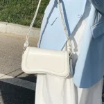 Sac à main Lina en similicuir blanc tenu à la main par une femme, disponible chez Boutique Izamel.