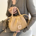 Sac à main Mia plissé crème tenu à la main par une femme, disponible chez Boutique Izamel.