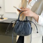 Sac à main Mia plissé noir tenu à la main par une femme, disponible chez Boutique Izamel.