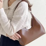 Sac à main Samia en similicuir marron porté à l'épaule par une femme, disponible chez Boutique Izamel.