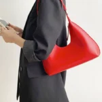 Sac à main Samia en similicuir rouge porté à l'épaule par une femme, disponible chez Boutique Izamel.